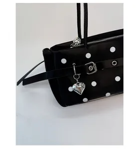 Detail of black polka dot shoulder bag with silver heart pendant and smooth leather texture