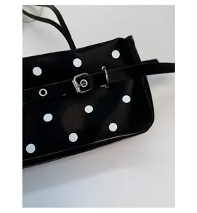 Detail of glossy black shoulder bag with white polka dots and silver metal buckle