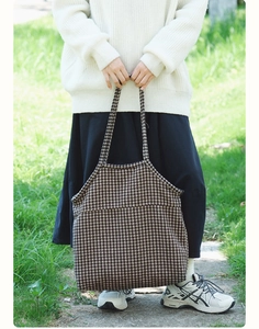 Detail of a houndstooth pattern tote bag held by a model in a natural outdoor setting