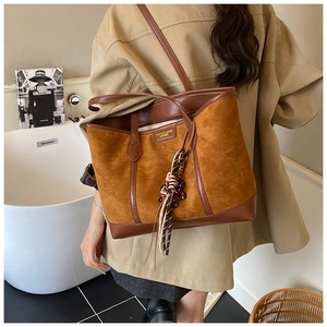 Detail of caramel suede tote bag with scarf charm and leather trim on a model