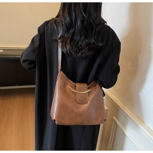 Detail of a brown leather shoulder bag featuring a gold crescent hardware and magnetic clasp