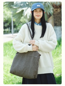 Outdoor lifestyle shot of a large houndstooth tote bag styled with a white sweater