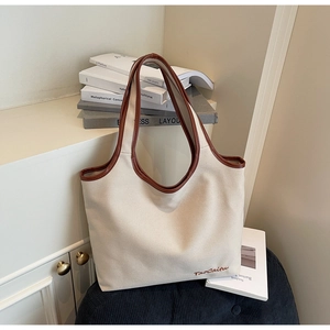 Detail of canvas tote bag showing brown leather trim and brand embroidery on white canvas