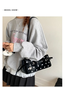 Close-up of black leather polka dot handbag with silver heart pendant on model