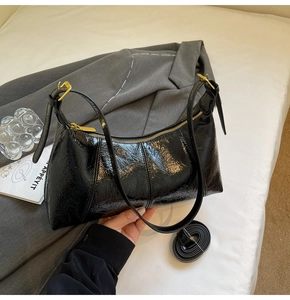 Détail du sac baguette en cuir verni noir avec fermeture éclair dorée et bandoulières