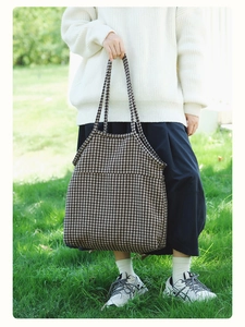 Outdoor lifestyle shot of a large houndstooth tote bag styled with a white knit sweater