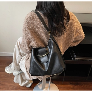 Detail of a black leather hobo bag with gold buckle and adjustable strap on a model