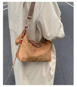 Brown suede tote bag with plush charm and bead tassel shown on model's shoulder