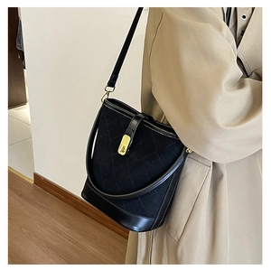 Close-up of a black quilted bucket bag with gold buckle on a beige trench coat