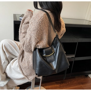 Close-up of black textured leather tote bag featuring a prominent gold curved metal clasp