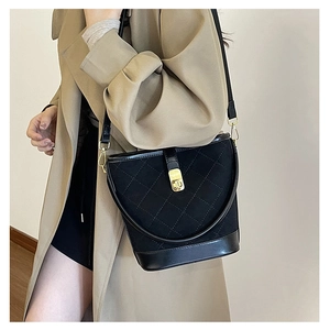 Close-up of black quilted bucket bag with gold clasp shown on a beige trench coat