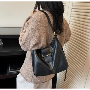Detail of a black leather tote bag with golden crescent buckle on a brown sweater