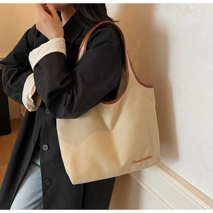 Detail of the large canvas tote bag featuring brown leather trim and TaoCaitu embroidery