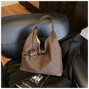 Close-up of a dark brown suede tote bag with leopard print charm on a leather chair