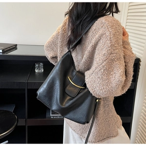 Detail view of a black faux leather shoulder bag with a gold curved metal buckle accent