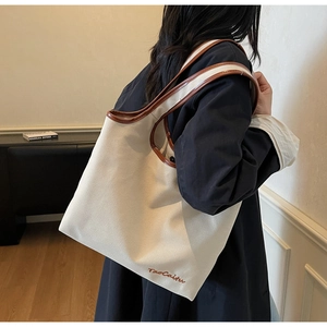 Detail of canvas tote bag showing red-brown leather trim and TaoCaitu embroidery