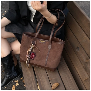 Detail of vintage brown tote bag with bear charm and tassel on outdoor bench
