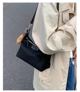 Detail of black canvas crossbody bag featuring leather logo tag and plush charm