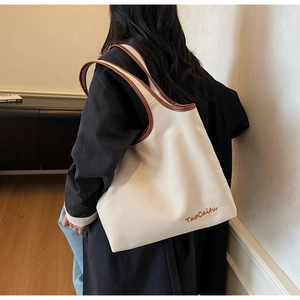 Detail of canvas tote bag featuring brown leather trim and TaoCaitu brand embroidery