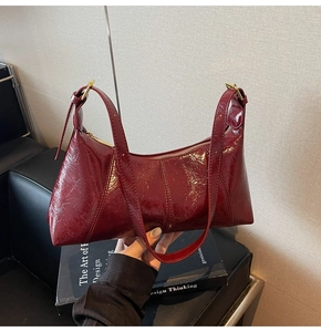 Détail du sac à main en cuir verni bordeaux avec boucles dorées sur un banc noir