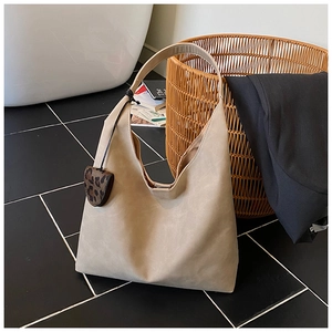 Detail of light khaki tote bag with leopard heart charm on elegant tiled floor