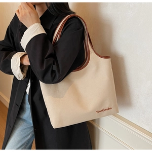 Detail of large canvas tote bag showing the embroidered logo and brown leather shoulder straps