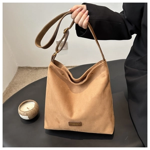 Detail of a brown suede hobo bag featuring an adjustable leather strap and brand logo plate