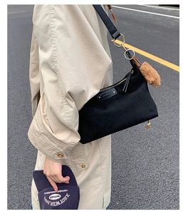Detail view of a black denim crossbody bag with plush charm and bead pendant in street style