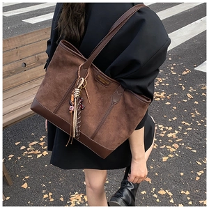 Detail of a brown suede tote bag with leather patchwork and a woven tassel charm