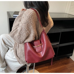 Detail view of burgundy tote bag with gold metal hardware on model in cozy interior