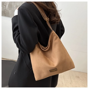 Detail of warm brown suede tote bag with adjustable bronze buckle and leather tag