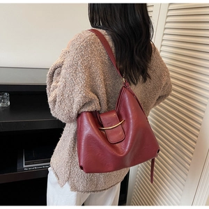 Burgundy faux leather shoulder bag with gold metal trim styled on a casual model