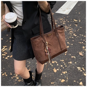 Detail of vintage brown suede tote bag featuring leather stitching and woven charm