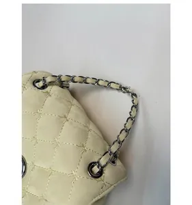 Dettaglio borsa trapuntata beige con ricamo a fiocco e manico a catena in metallo