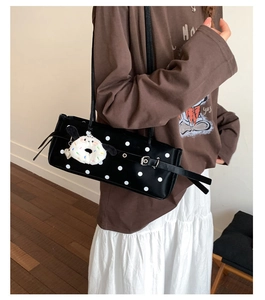 Detail of black polka dot underarm bag with silver buckle and white plush charm