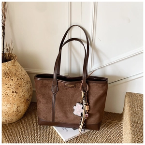 Detail of brown suede tote bag with pink bear charm on straw mat background