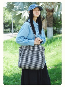 Classic houndstooth knit tote bag with wide shoulder strap shown in an outdoor park setting