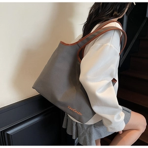 Close-up of charcoal grey canvas tote bag with brown leather trim and TaoCaitu embroidery