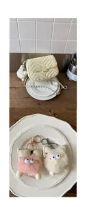 Details einer cremefarbenen Stepptasche mit Metallkette und Plüschmonster-Anhängern