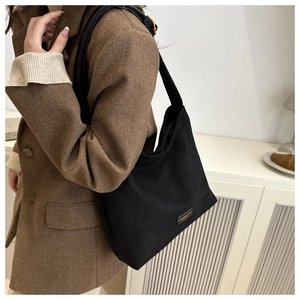Detail of black matte tote bag with adjustable leather strap and tiny metal nameplate