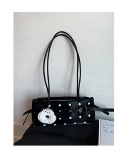 Close-up of black polka dot baguette bag with metal grommets and white plush charm