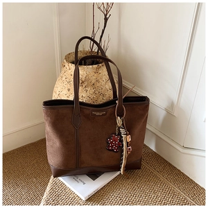 Close-up of brown suede tote bag featuring metallic fashion logo and leopard bear charm