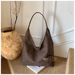 Detail of dark brown suede tote bag featuring a leopard heart charm and side drawstrings