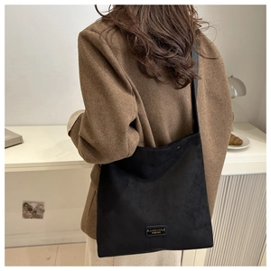 Close-up of black matte tote bag with embossed leather label detail worn by model