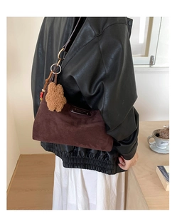 Detail of dark brown suede shoulder bag with a plush bear charm on a female model