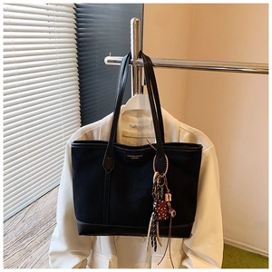 Detail of black tote bag featuring leather trim, tassel charm, and logo text on the front