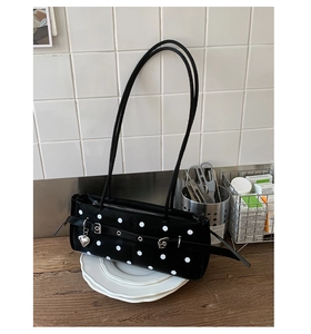 Detailed view of polka dot baguette bag with silver heart pendant on white tile background