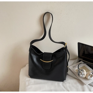 Close-up of black matte shoulder bag featuring a gold crescent-shaped metal buckle on the front