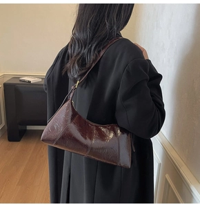Close-up of a retro dark brown glossy leather dumpling bag worn on a shoulder