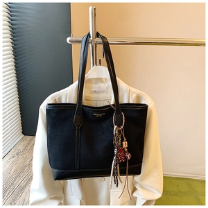 Close-up of black tote bag with suede texture, gold lettering and tassel charm detail
